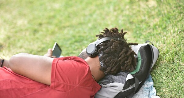 Black man laying in the grass wearing autism noise canceling headphones